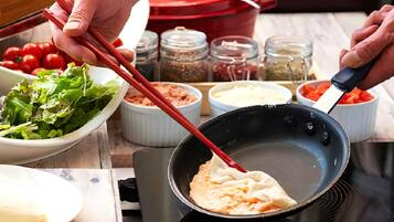 A person cooking with a pan on a stove, surrounded by bowls of food and ingredients.