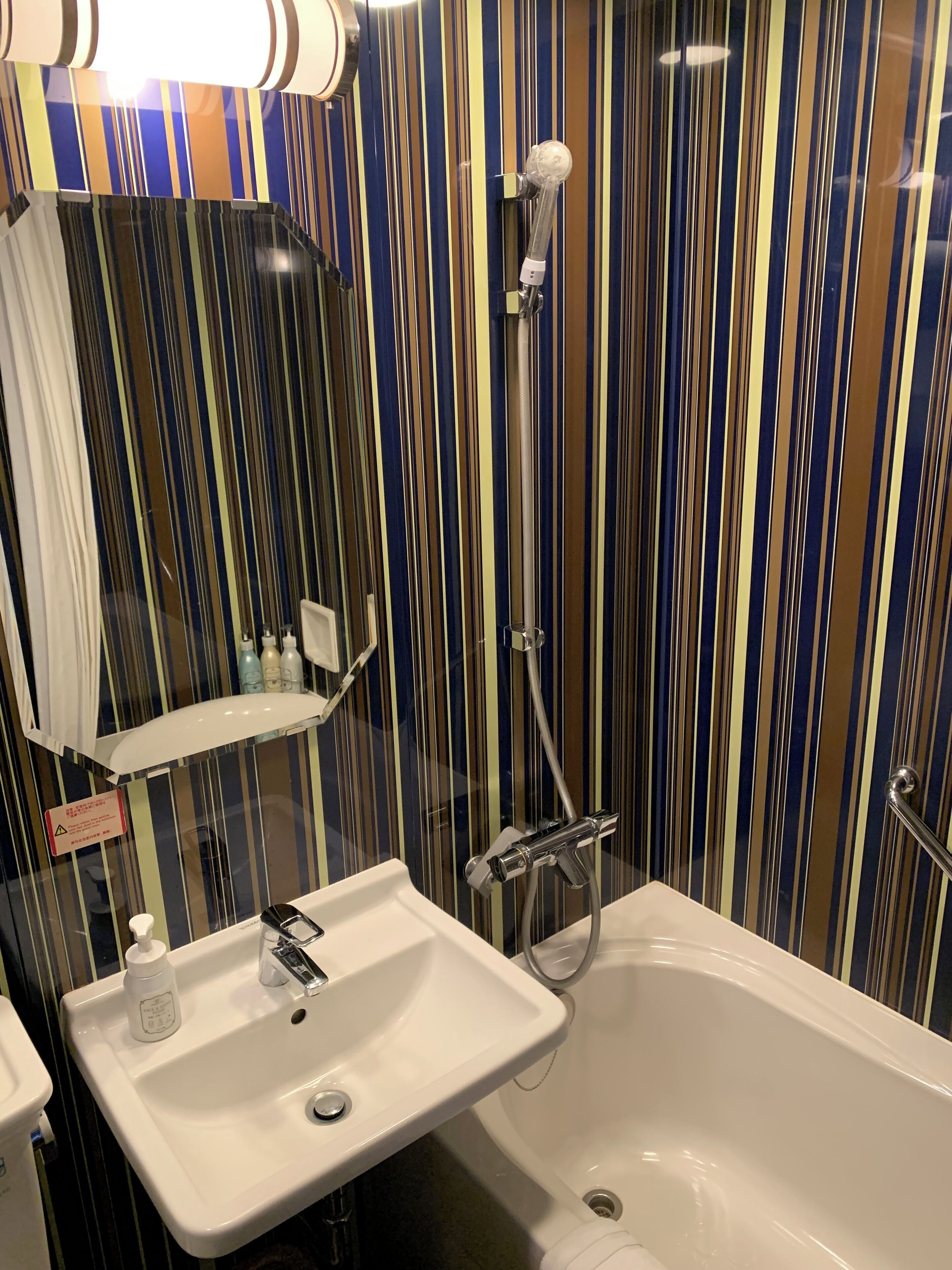 Un baño con un lavamanos blanco, un espejo, ducha y paredes a rayas.