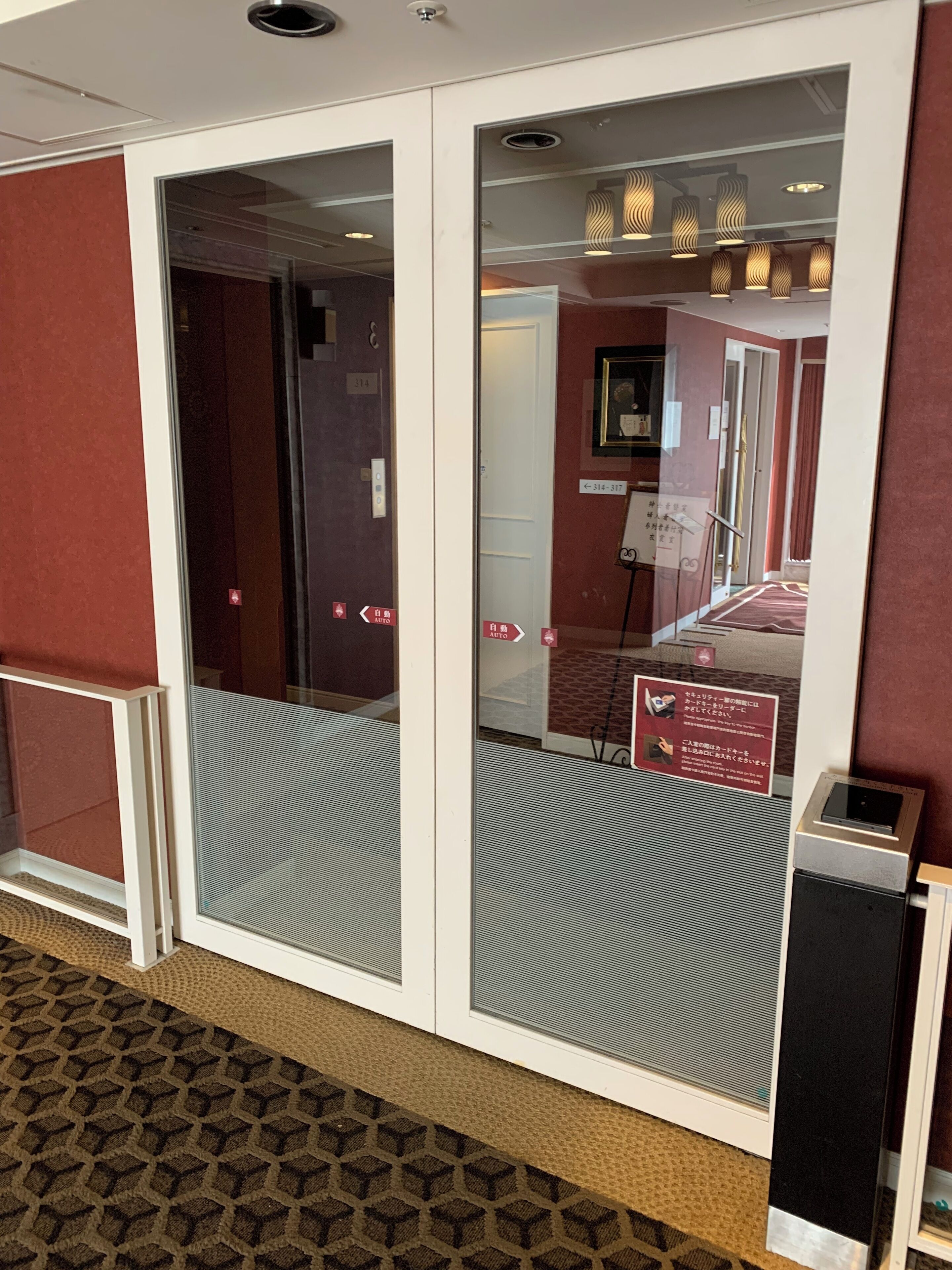 A hotel entrance with a glass door, a sign indicating room availability, and a digital keypad.