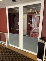 A hotel entrance with a glass door, a sign indicating room availability, and a digital keypad.