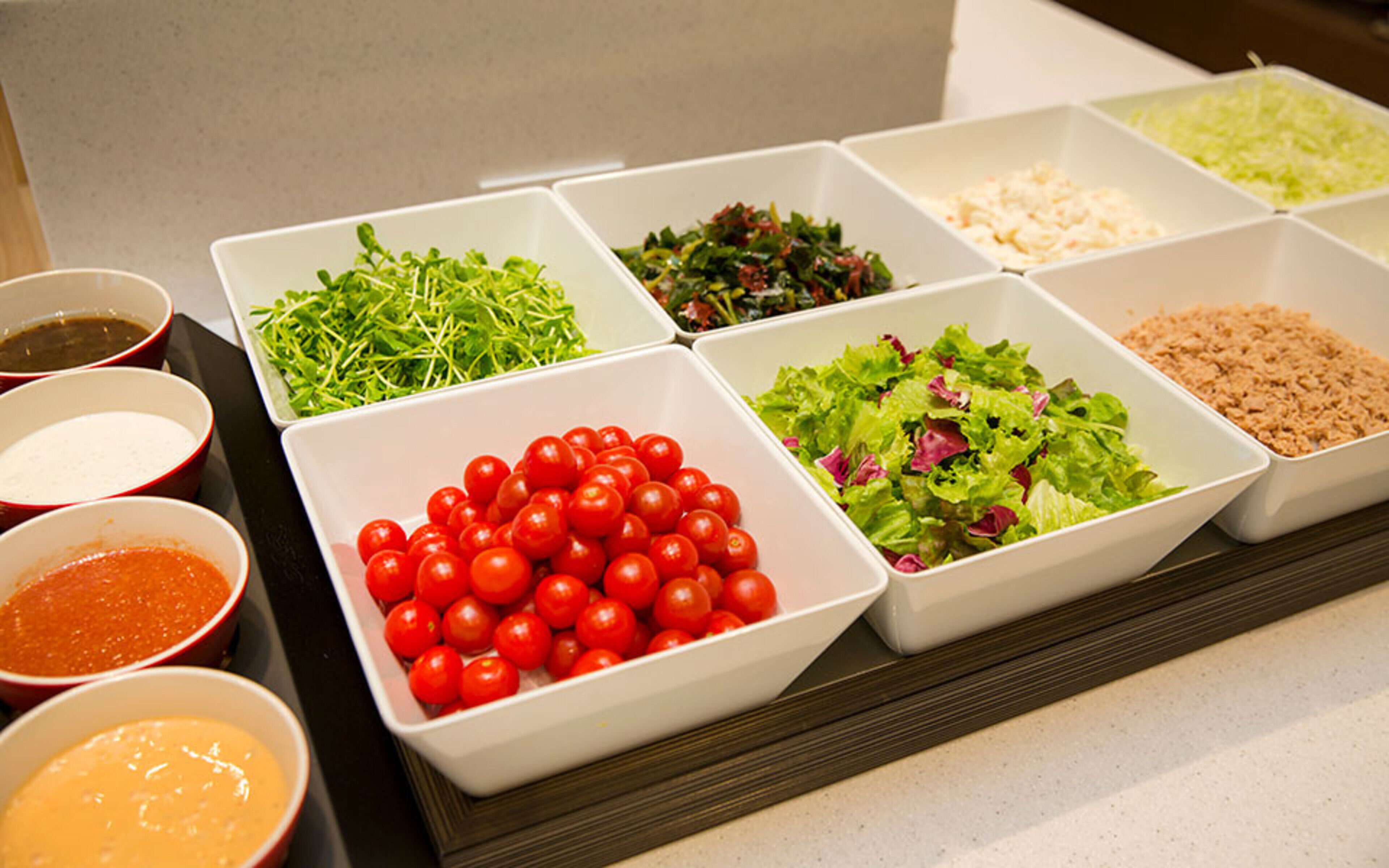 A buffet with various food items including salads, cherry tomatoes, and different sauces.