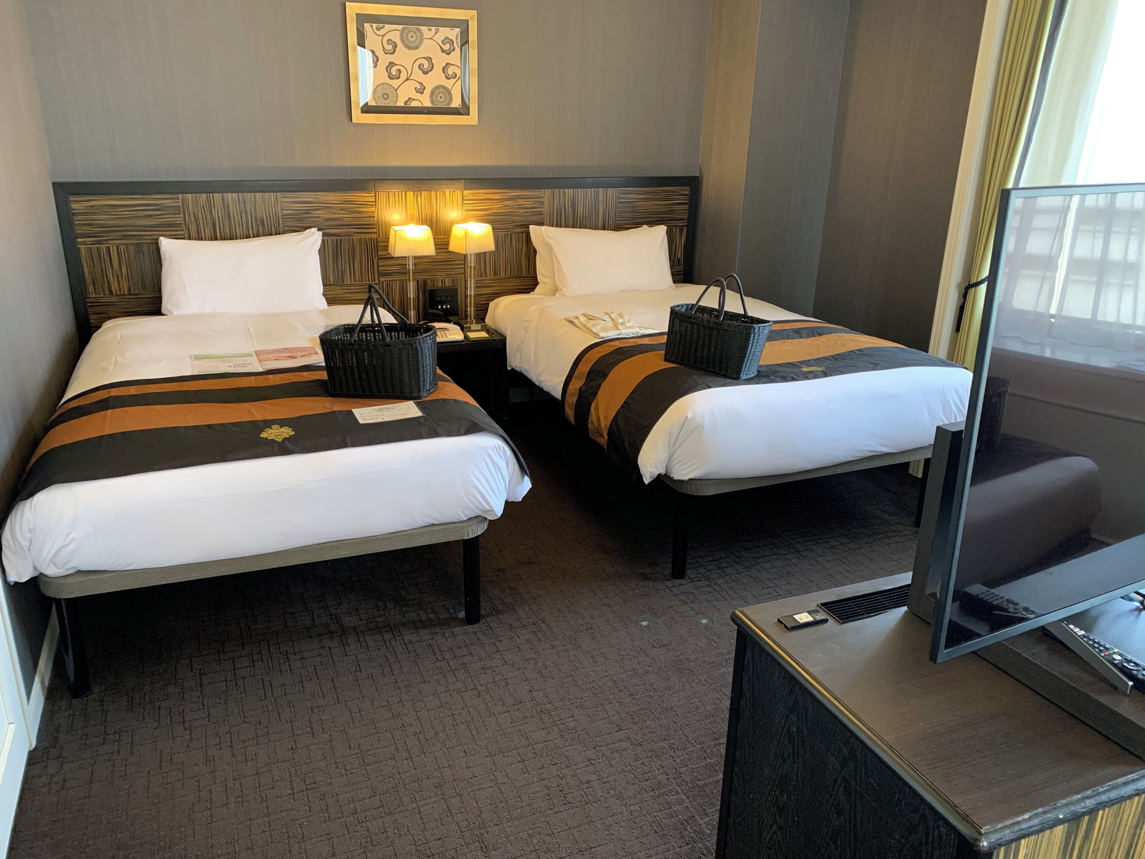 A hotel room with two beds, a TV, and a bedside table.