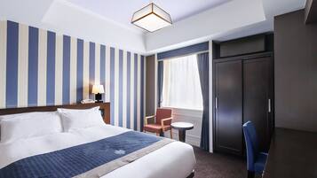 Habitación de hotel con una cama grande, un escritorio, una silla, un armario y una ventana con cortinas.
