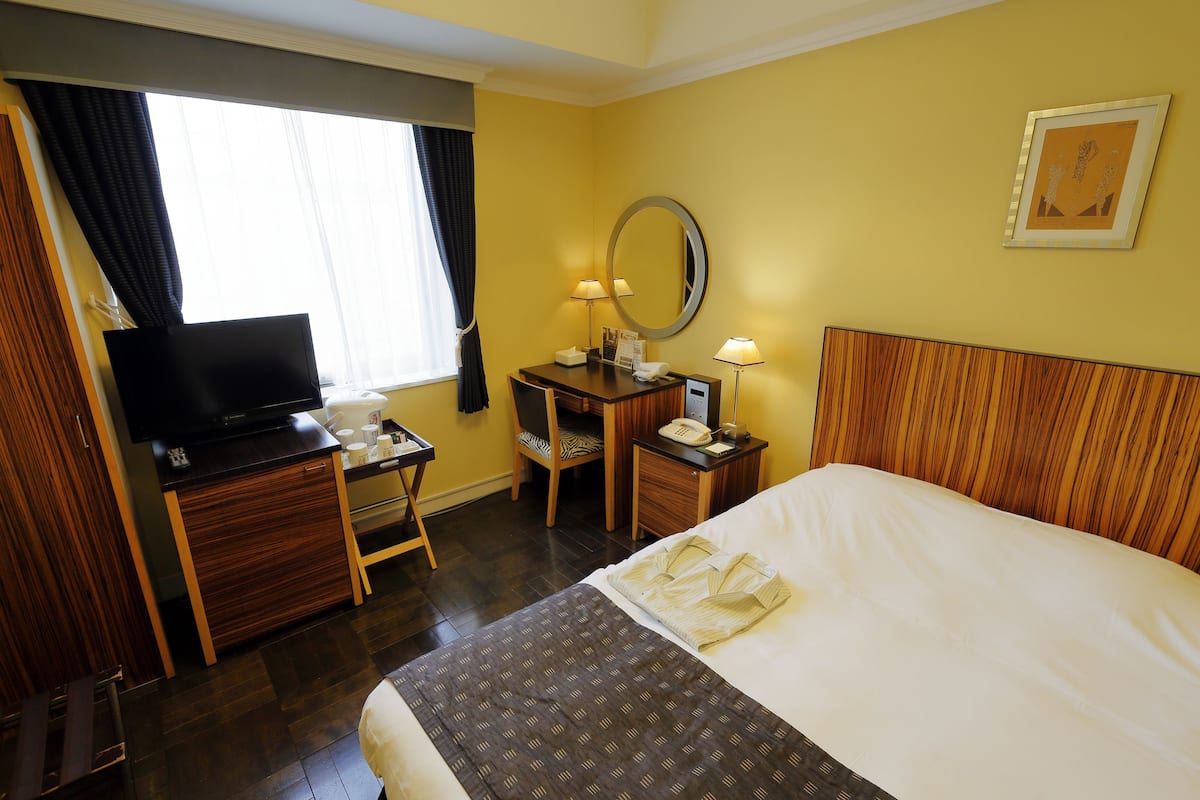 Une chambre d’hôtel comprenant un lit, un bureau avec une chaise, une télévision, un miroir et une fenêtre avec des rideaux.