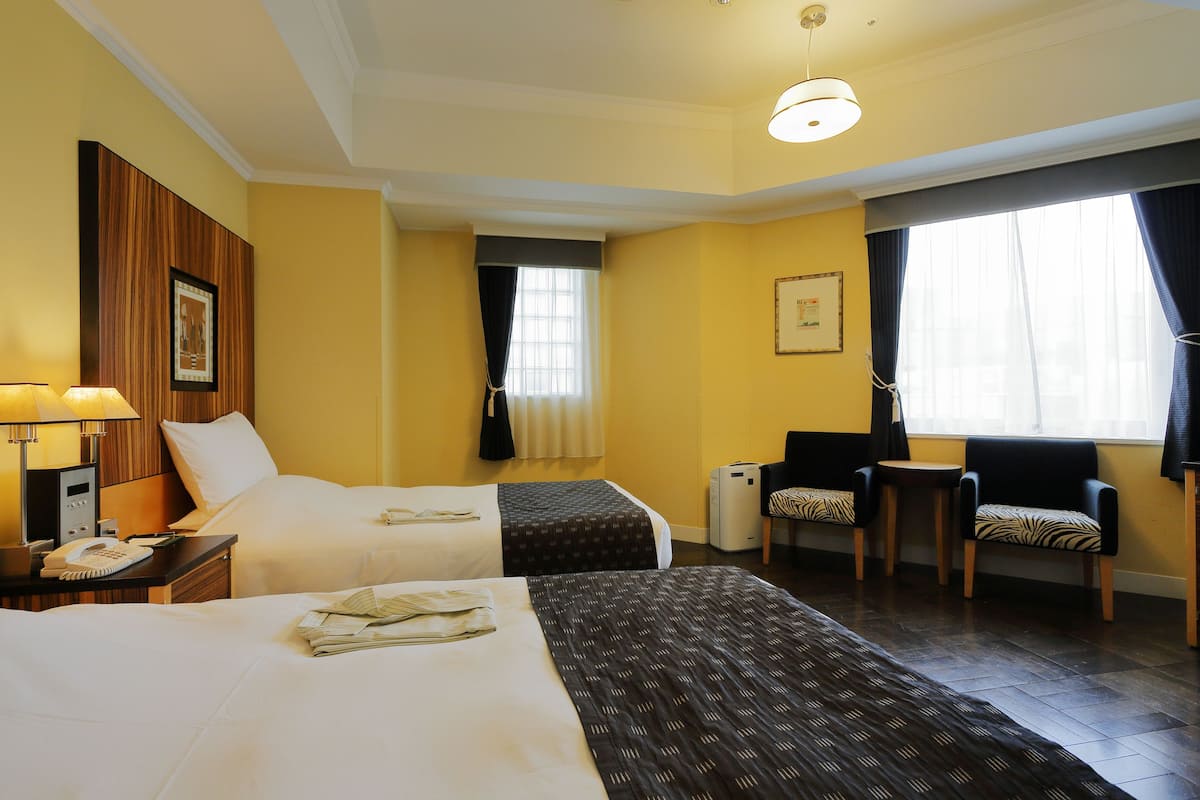Une chambre d’hôtel avec deux lits, un bureau avec une lampe, une chaise et une petite table.