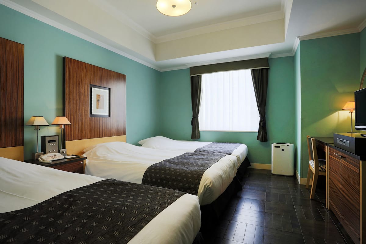 Une chambre d’hôtel avec deux lits, un bureau, une chaise, une télévision, un téléphone et une poubelle.