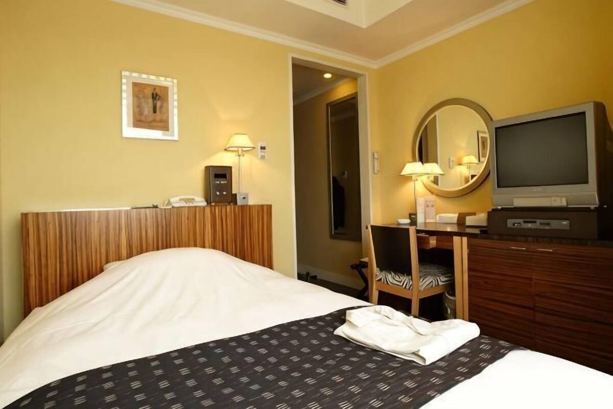 Une chambre d’hôtel comprenant un lit, une table de chevet, une lampe, une télévision et un miroir.