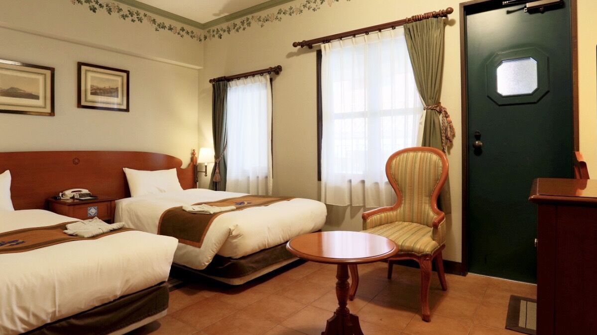 Een hotelkamer met twee bedden, een tafeltje, een stoel, een bureau en een deur.