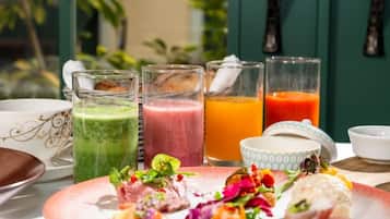 A table with a variety of food items and drinks, including a green smoothie, a pink smoothie, and a glass of orange juice.