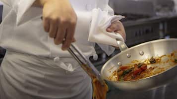 Een kok in een witte uniform met een hoge koksmuts roert eten in een professionele keuken.