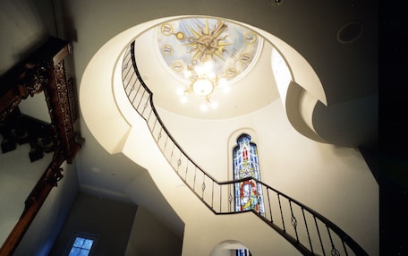 A spiral staircase with a clock at the top, a stained glass window, and a wooden sculpture.