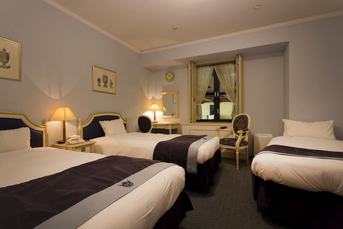 A hotel room with two beds, a desk, a chair, a clock, and framed pictures on the wall.