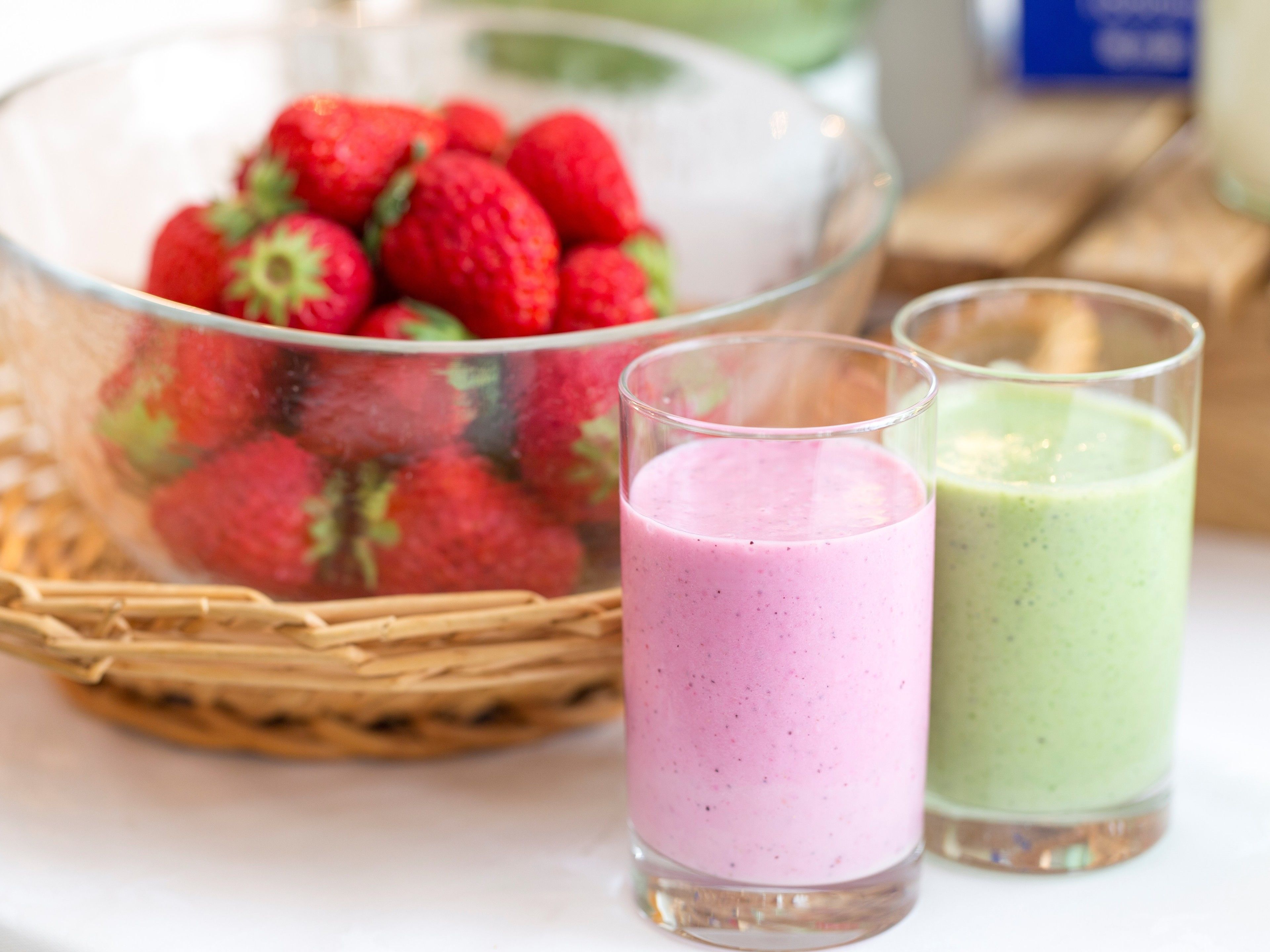 Dos vasos de smoothie y un bol de fresas.