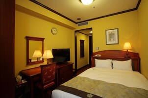 Habitación de hotel con cama, escritorio con televisor, espejo, reloj y un cuadro en la pared.
