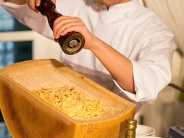 Um chef despejando molho em uma panela de cozimento grande e retangular.
