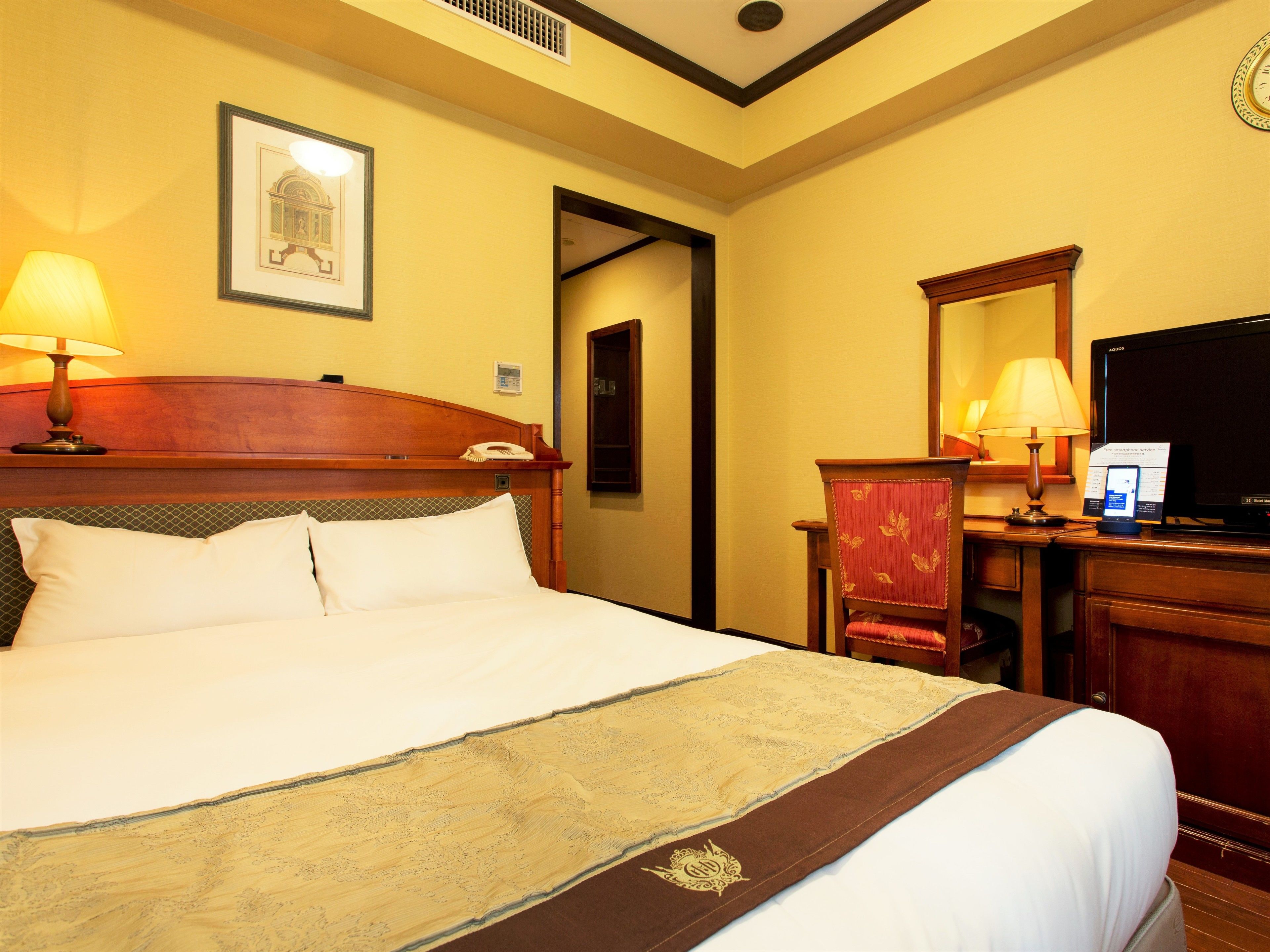 A hotel room with a large bed, a desk with a computer, a telephone, and a television.