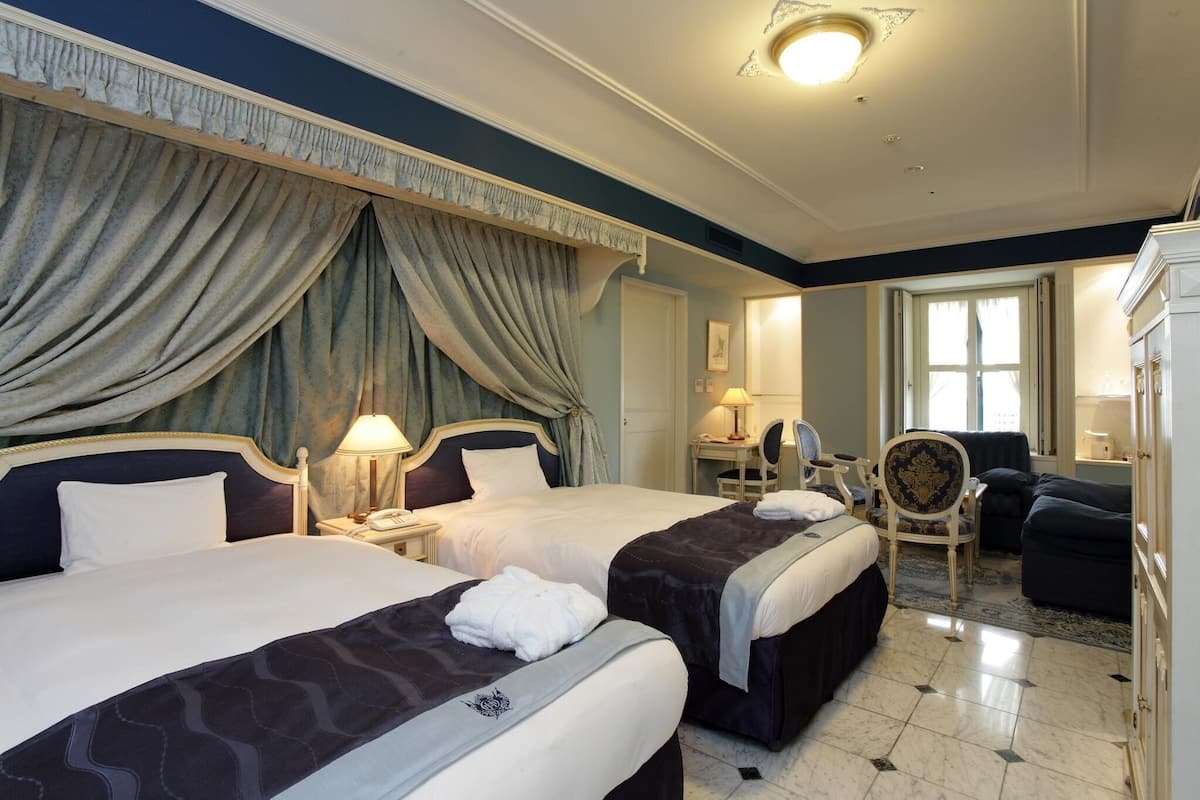A hotel room with two beds, a desk, a chair, and a sofa.