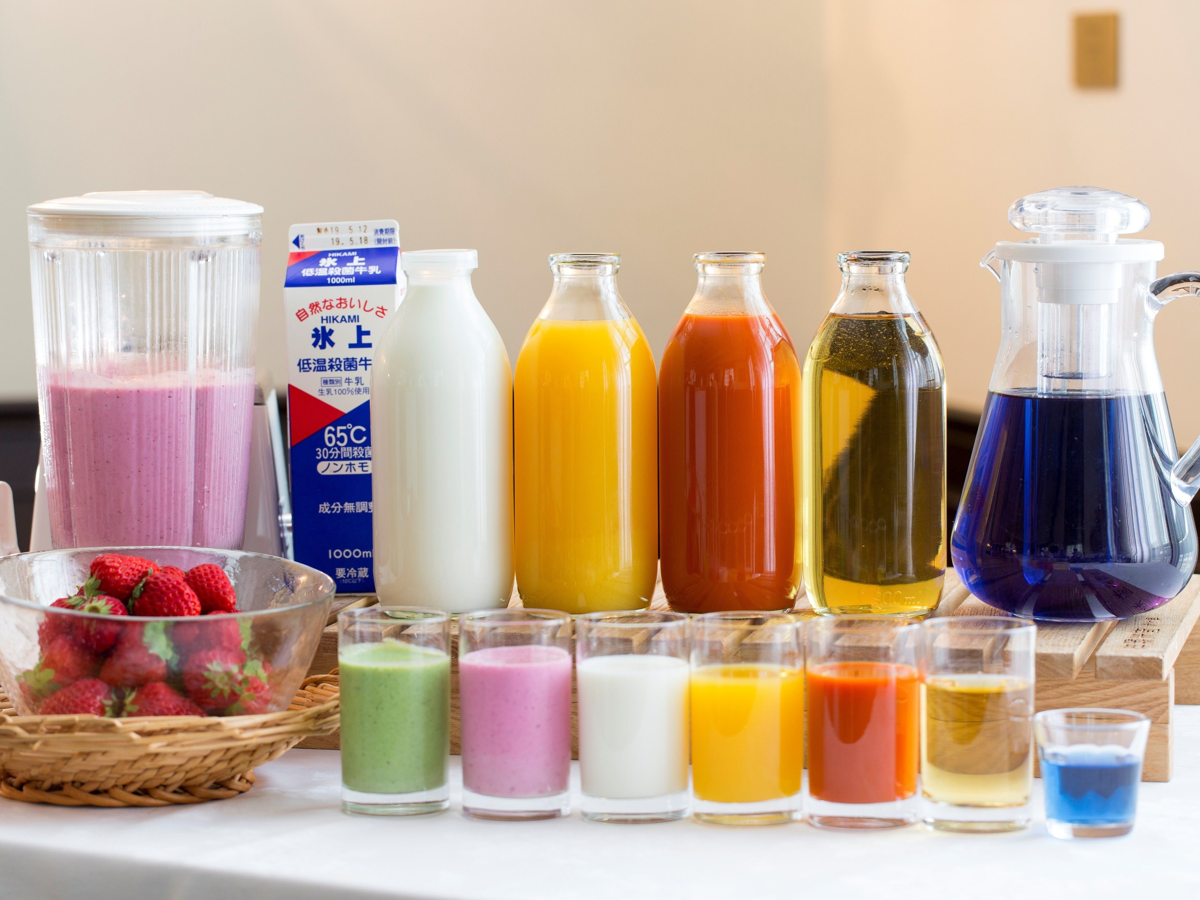 A variety of beverages in different containers, including a blender, bottles, and a pitcher, arranged on a table.