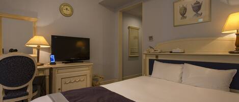 Una habitación de hotel con una cama, un escritorio con televisor, una silla, un reloj y un cuadro en la pared.