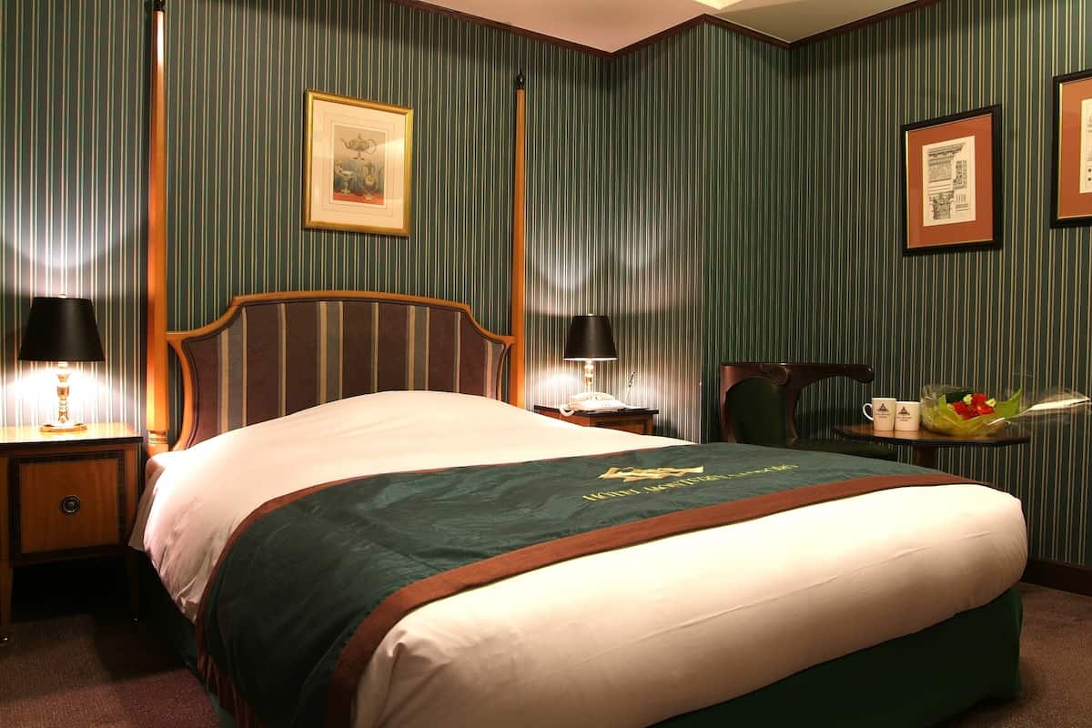 A hotel room with a large bed, two bedside tables with lamps, a small table with a vase and a mug, and a framed picture on the wall.