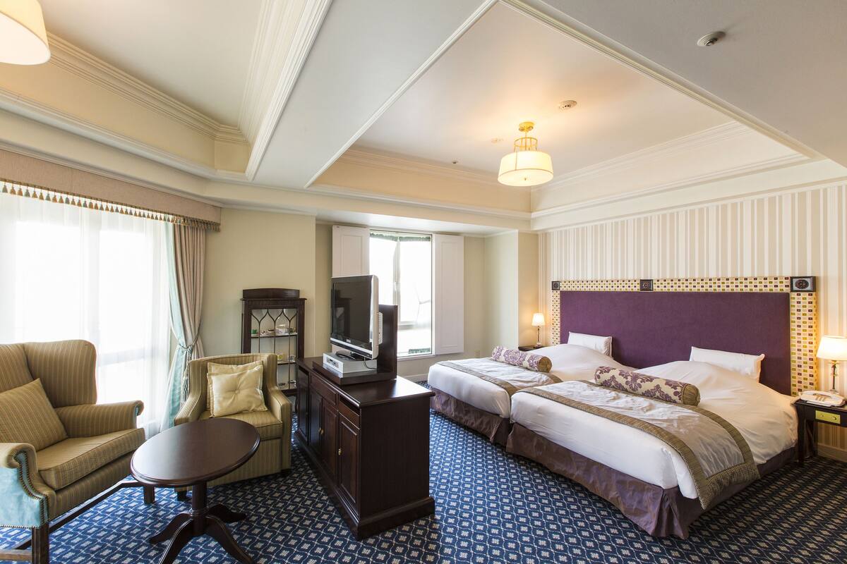 A hotel room with a large bed, a sofa, a desk, and a television.