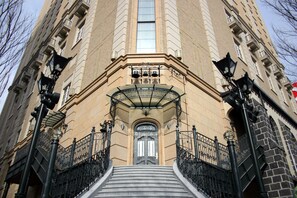 A building with a grand entrance, featuring a large arched doorway, a set of stairs leading up to it, and a balcony with a wrought iron railing. - Hotel Monterey Sendai (Sendai)