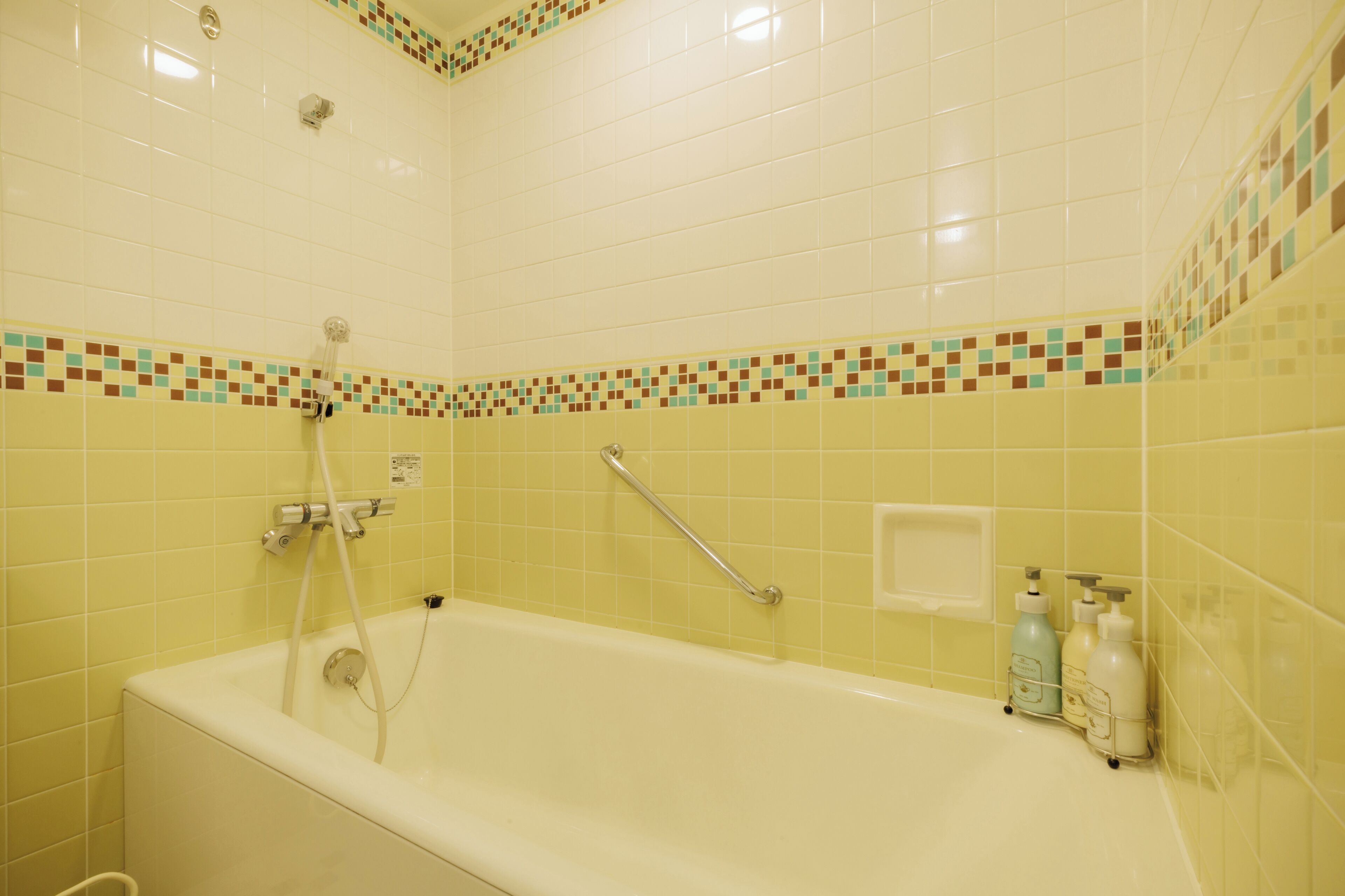 Une salle de bain avec une baignoire, une barre d’appui et un mur carrelé agrémenté d’une bordure décorative.