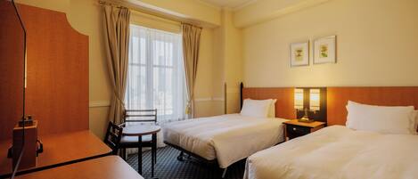 A hotel room with two beds, a desk, a chair, and a window with curtains.