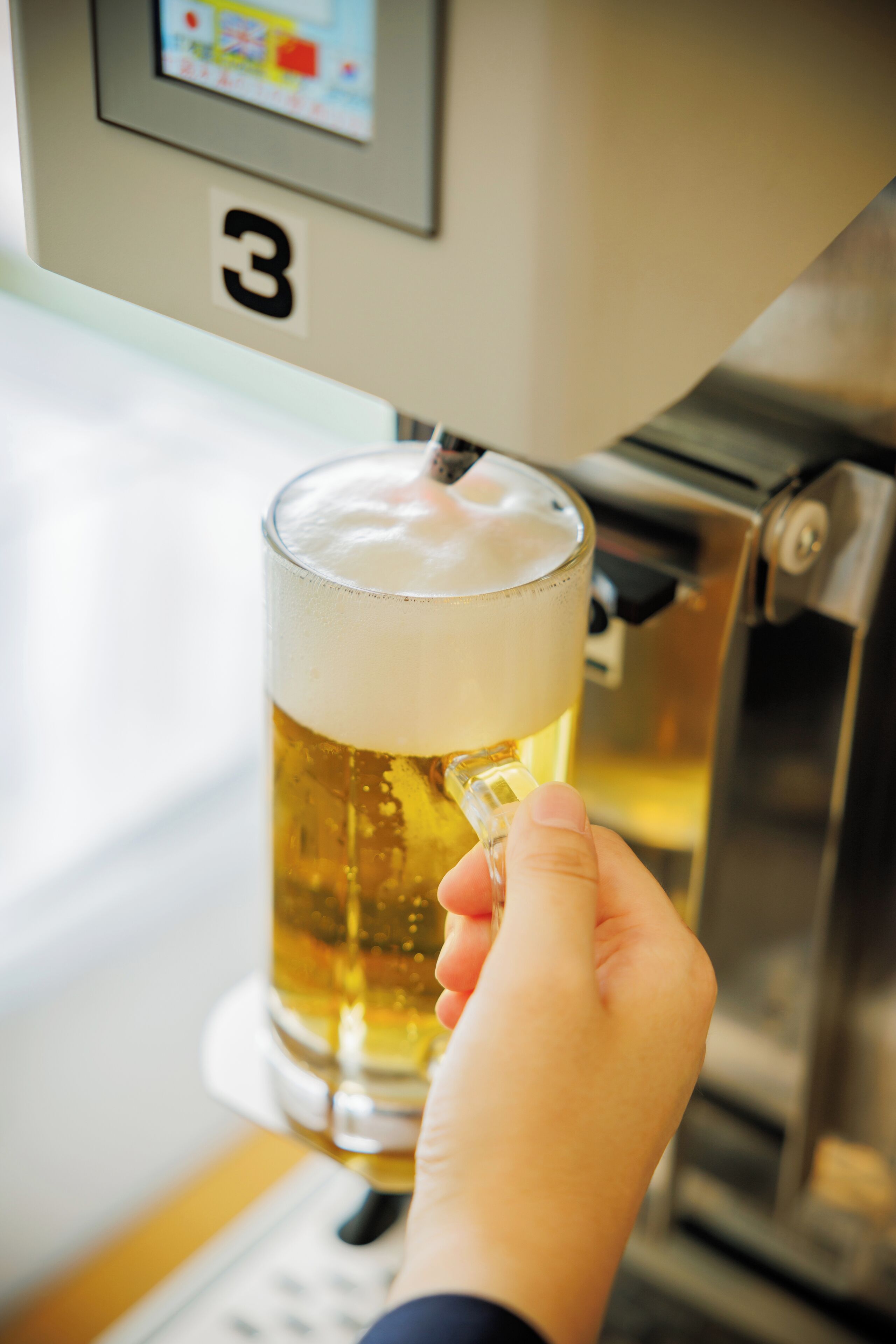 Una mano sosteniendo un vaso de cerveza con espuma, frente a una llave de cerveza etiquetada con el número 3.