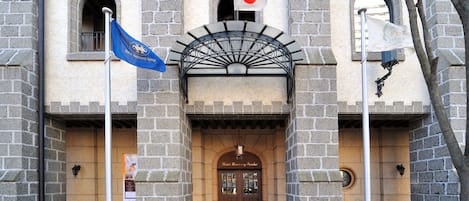 Ein historisches Gebäude mit einer Sandsteinfassade, bogenförmigen Fenstern und einem zentralen Eingang mit der Beschriftung 'Hotel Rosenau'.