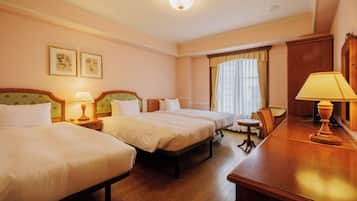 A hotel room with two beds, a desk, a chair, and a small table.