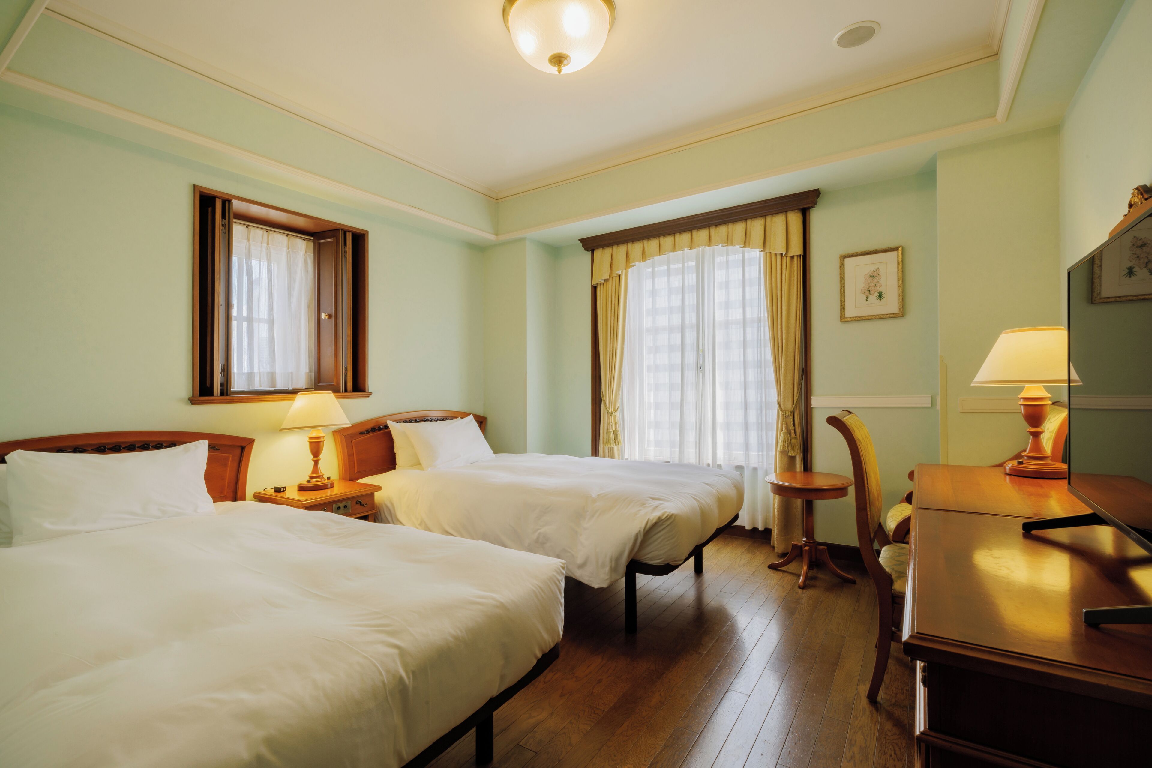 A hotel room with two beds, a desk, a chair, and a lamp.