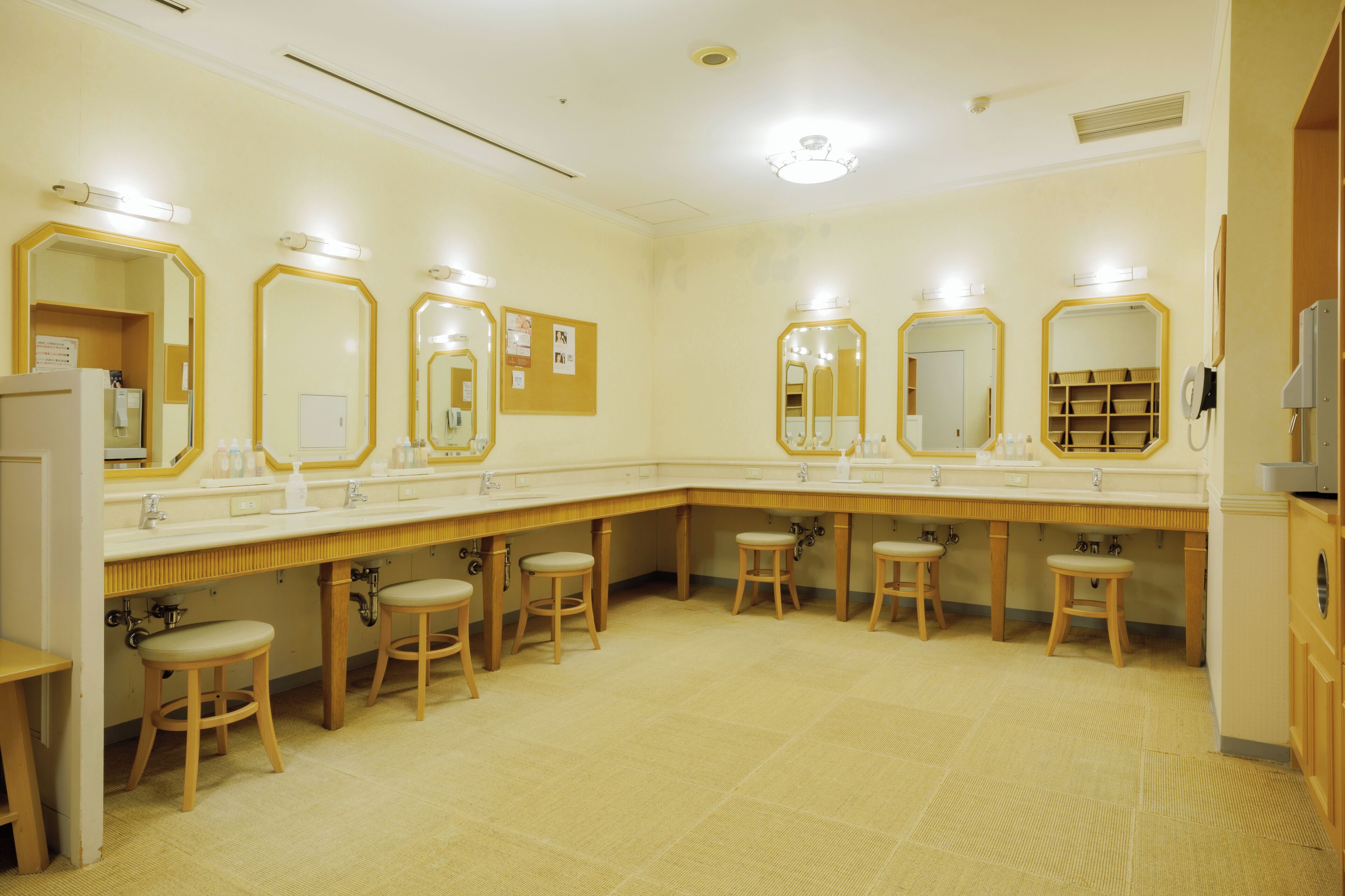Un baño público con varios lavamanos, espejos y taburetes de madera.