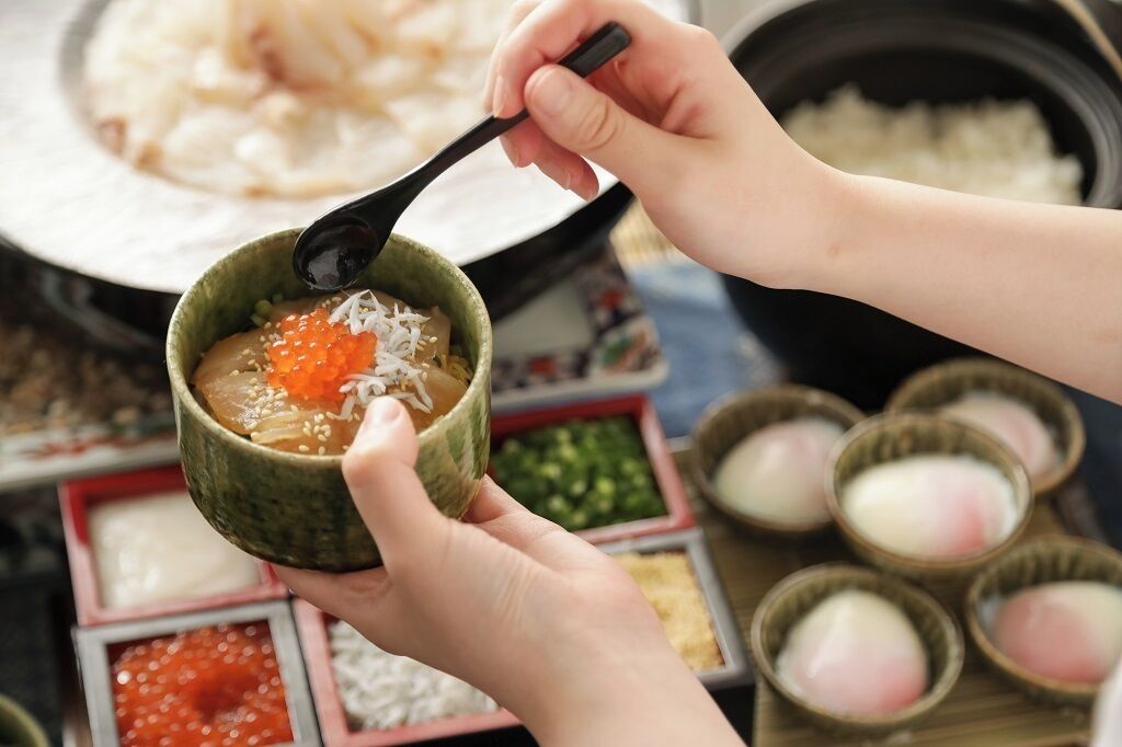A person holding a bowl with a spoon, containing a dish with orange fish roe and white rice.