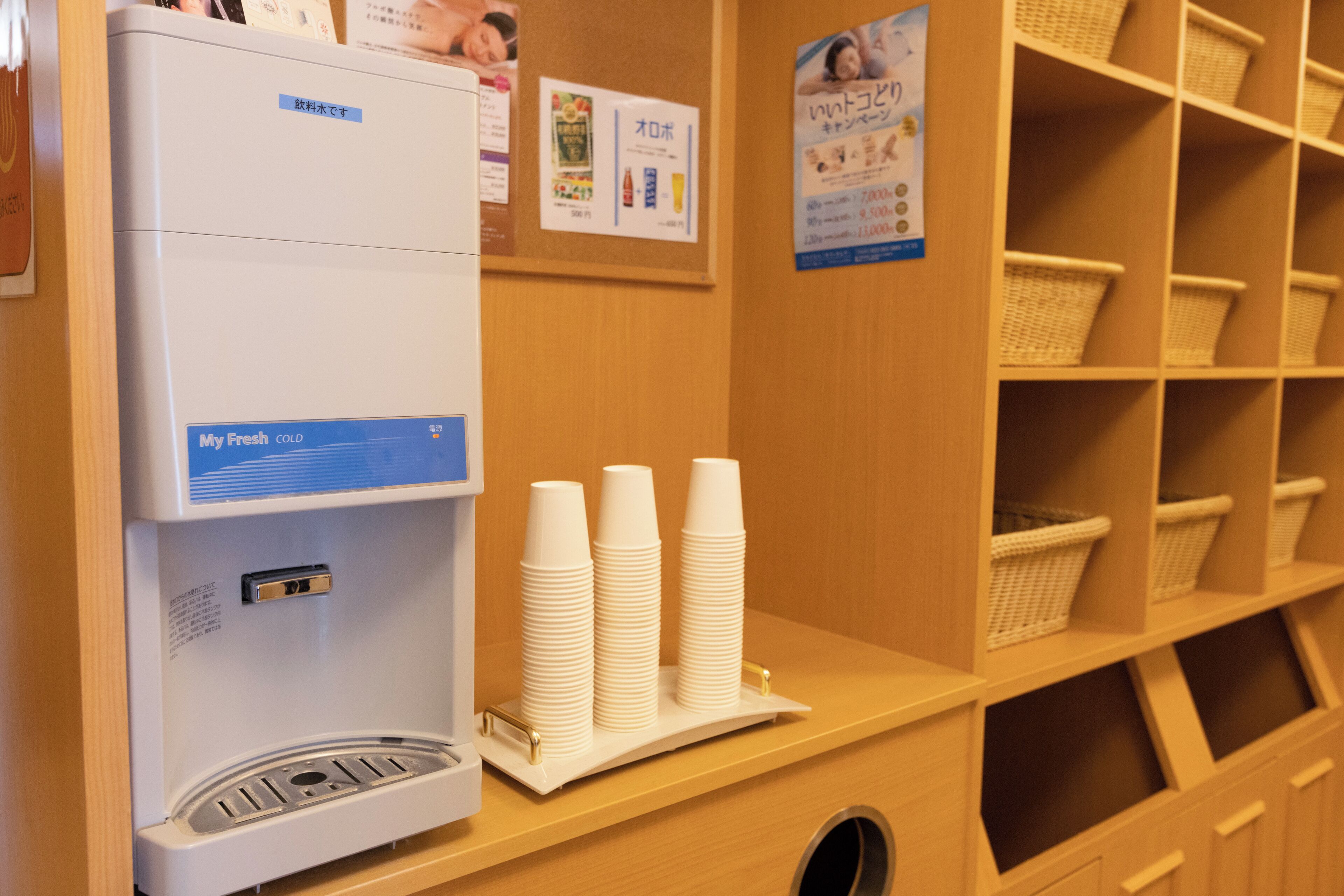 Una máquina de café con pantalla digital, vasos de papel apilados y estantes con cestas.