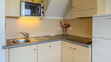 A compact kitchen with a built-in microwave, a stainless steel sink, and wooden cabinets.