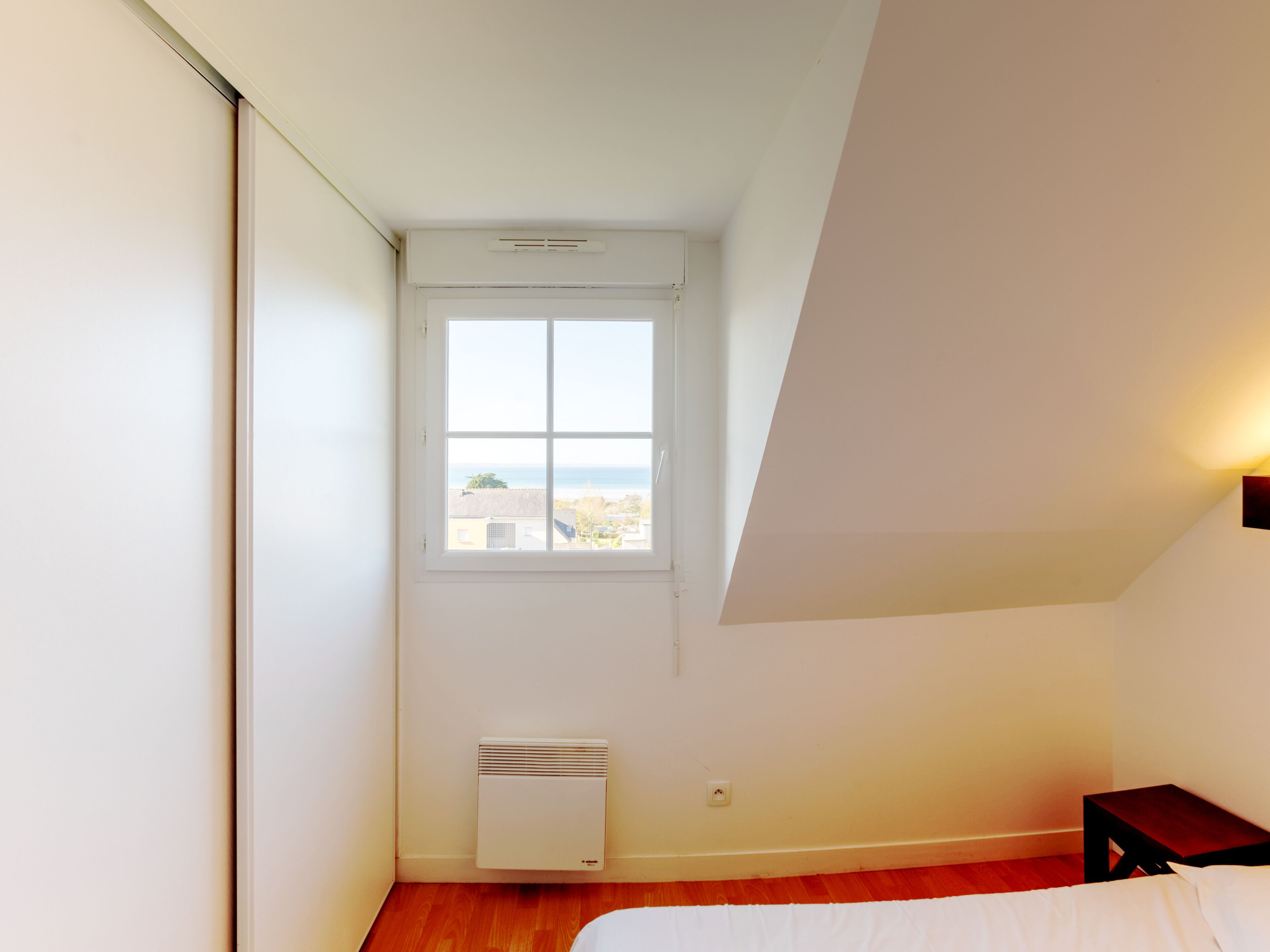 A bedroom with a window, a radiator, and a bedside table.