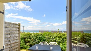 Un patio exterior con una mesa y sillas, una cerca de madera y vista al mar.