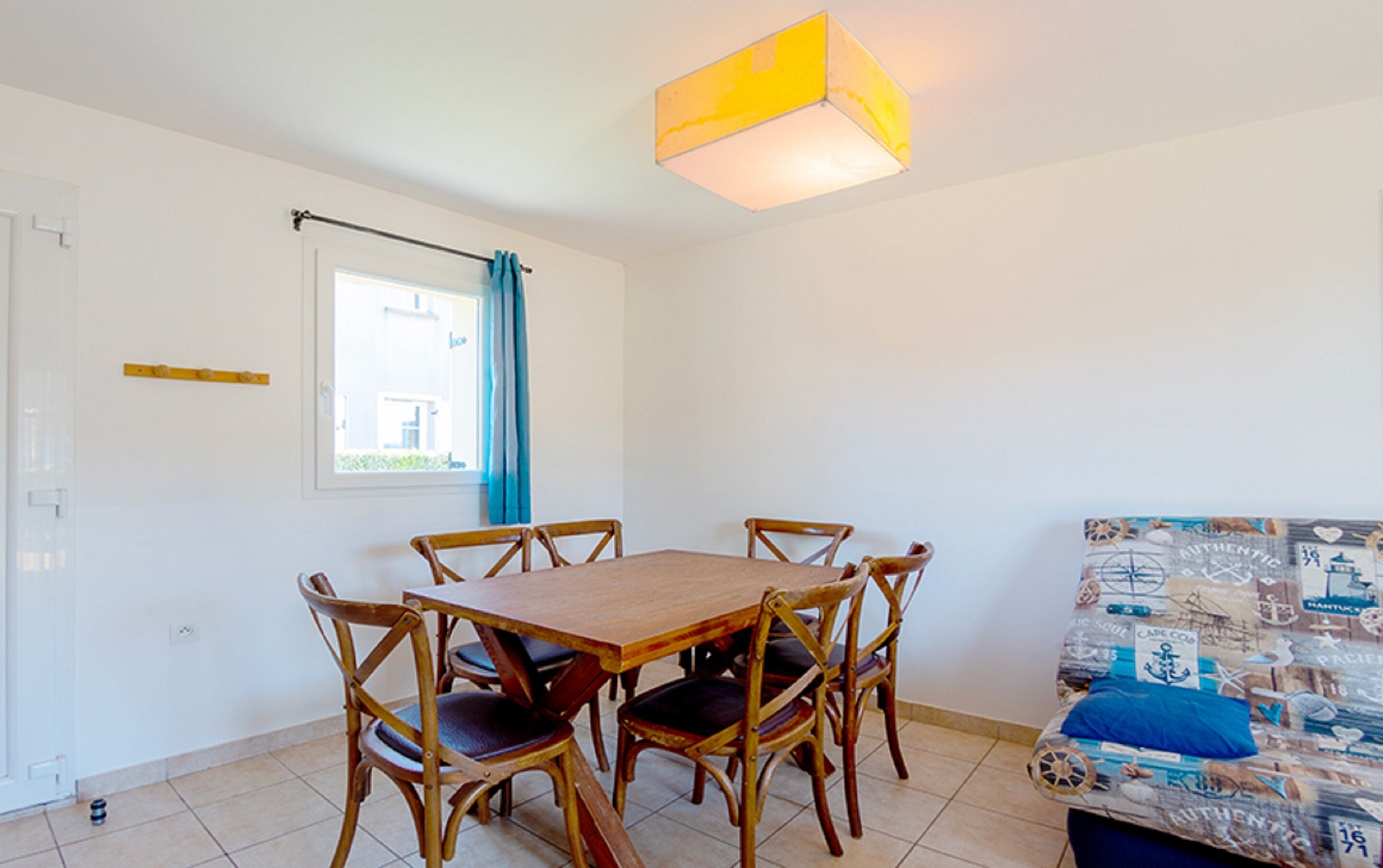 A dining area with a wooden table and chairs, a window with a curtain, and a sofa with a patterned cover.