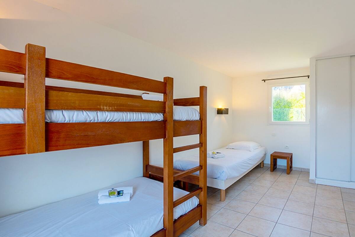 Una habitación con dos literas, una cama individual, una mesita de noche pequeña y una ventana con vistas a zonas verdes.