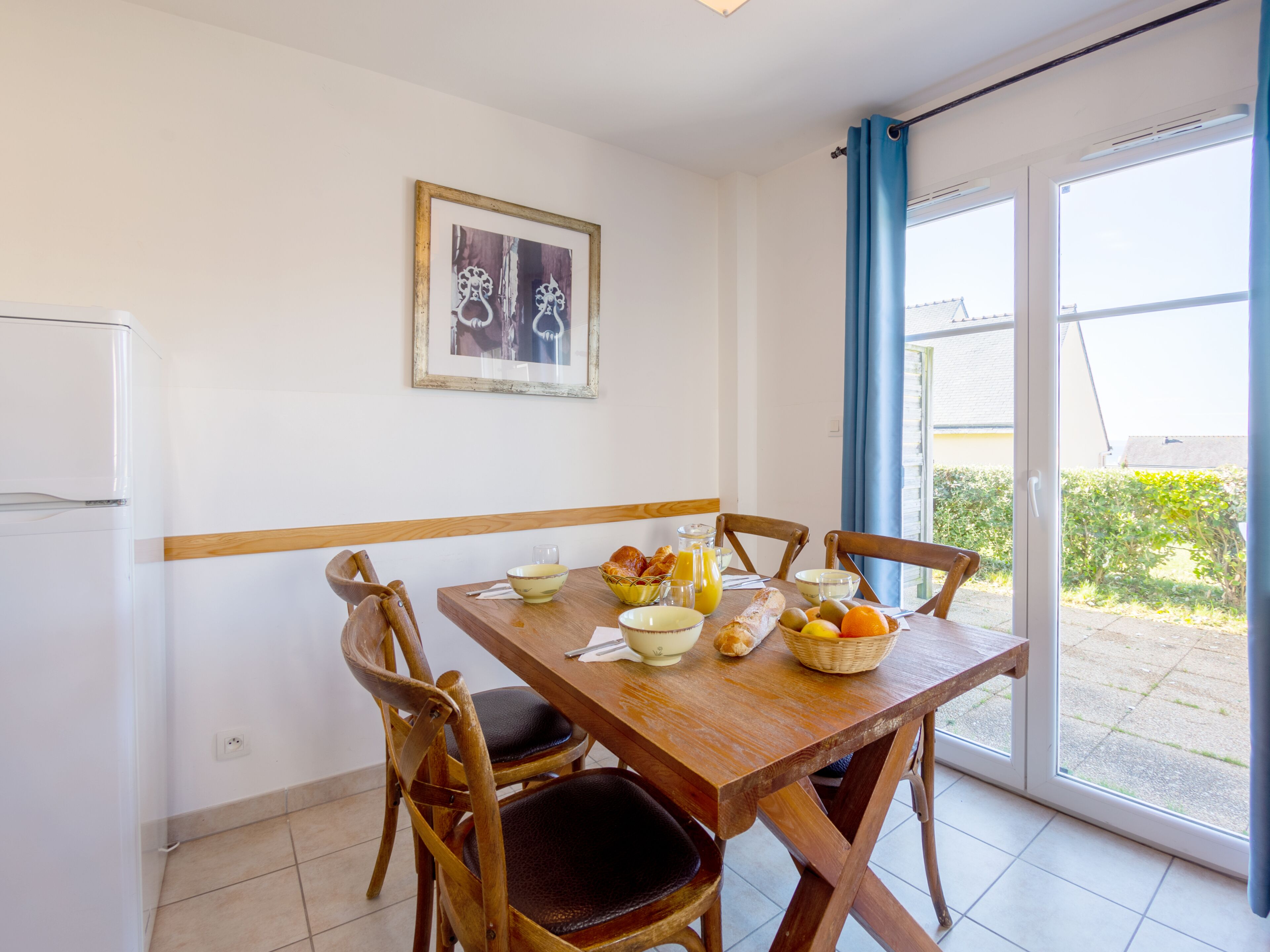A dining area with a wooden table set for breakfast, including bread, fruit, and a bowl of cereal.