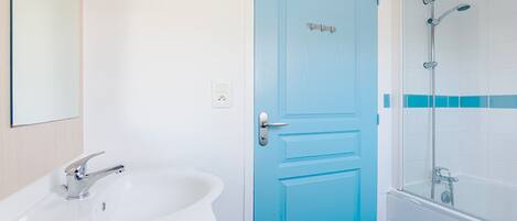 Een badkamer met een wit wastafelmeubel, een blauwe deur en een douchecabine.