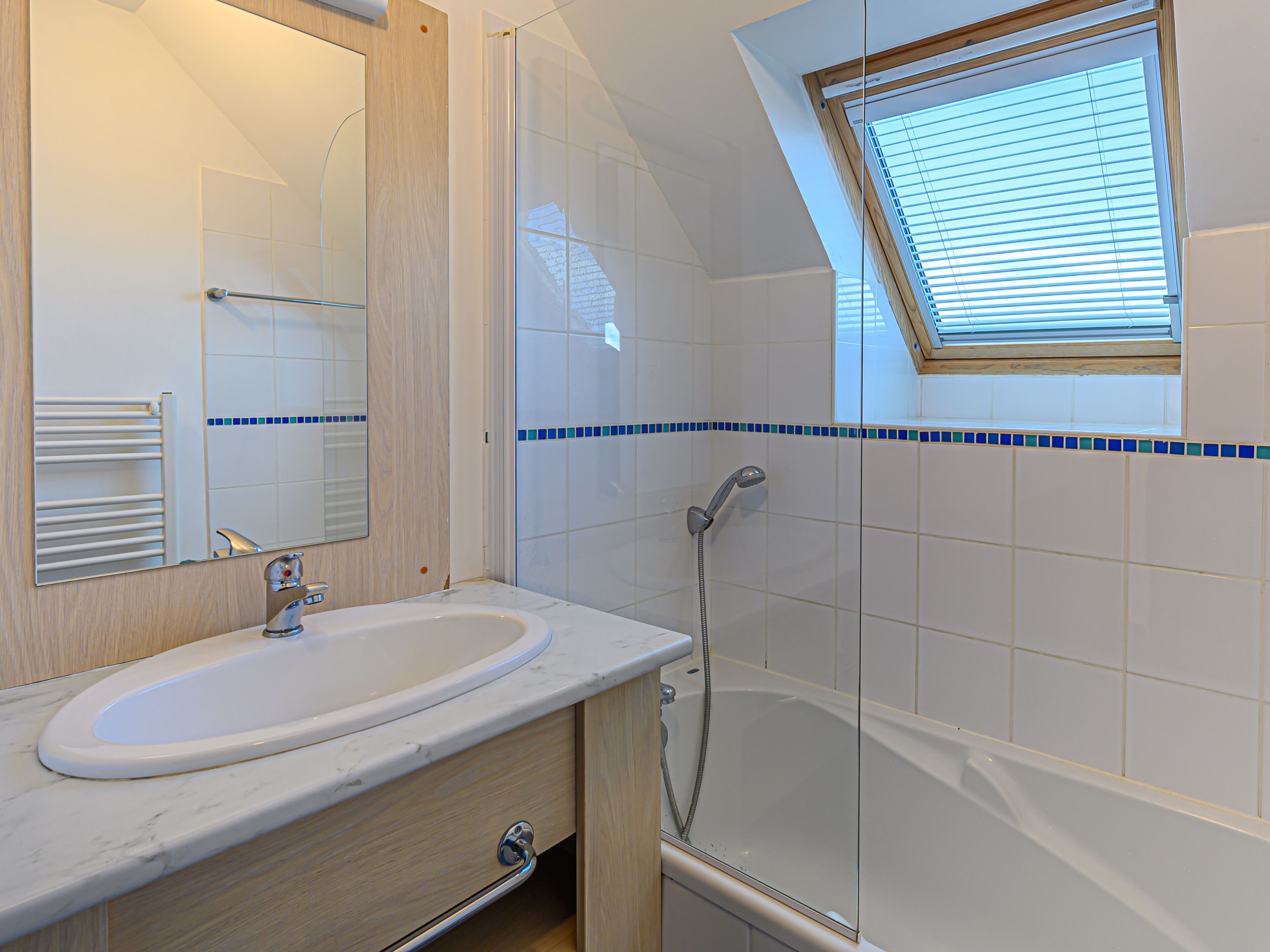 A bathroom with a white sink, a mirror, a shower, and a skylight.