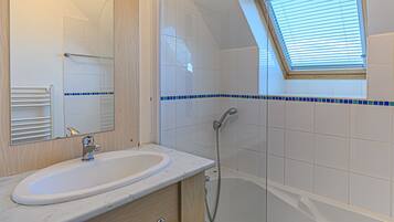 A bathroom with a white sink, a mirror, a shower, and a skylight.