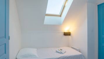 A small, single-bed room with a skylight, a wall-mounted light, and a radiator.