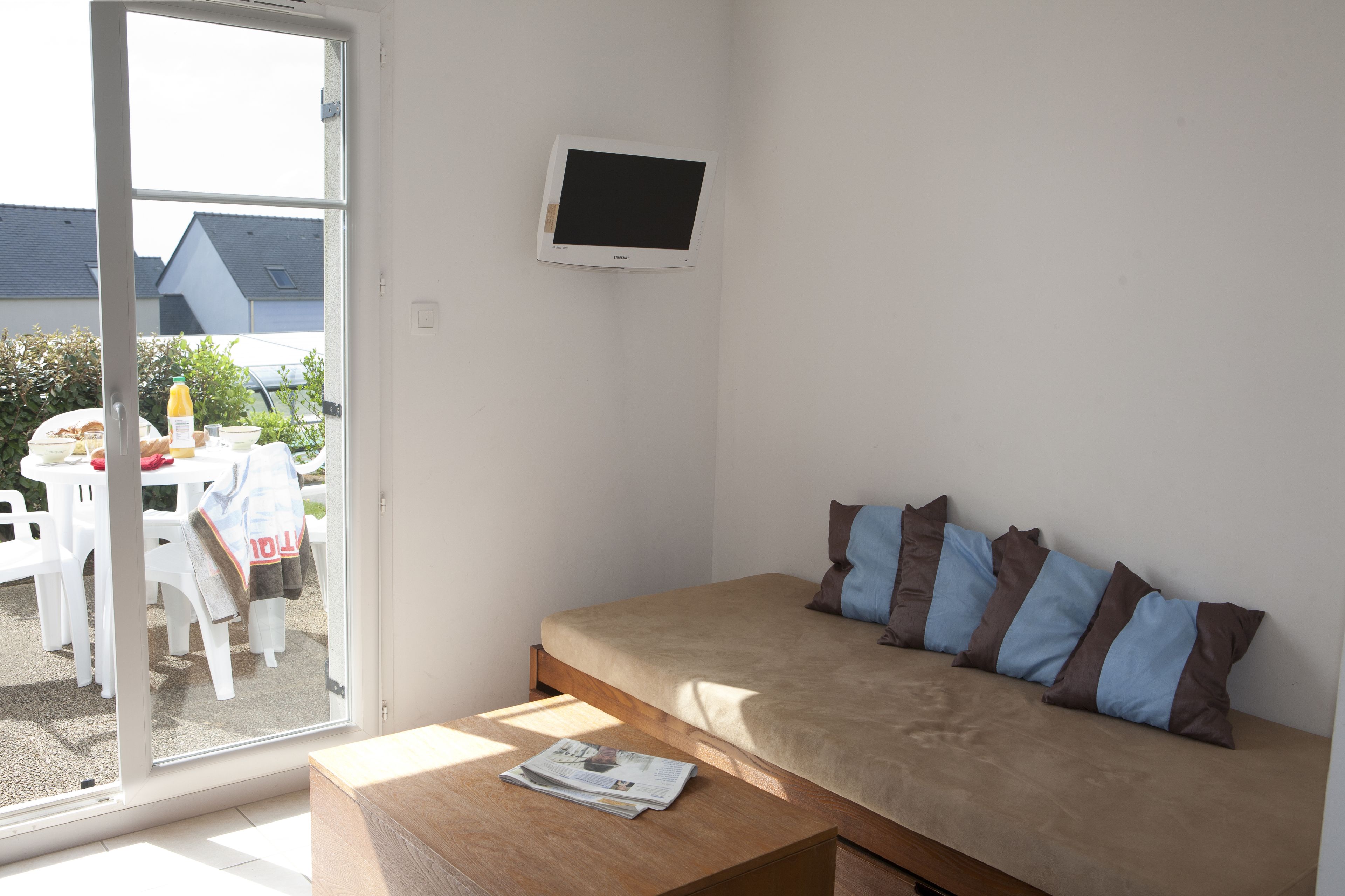 A bedroom with a bed, a TV mounted on the wall, a wooden table, and a window with a view of the outside.