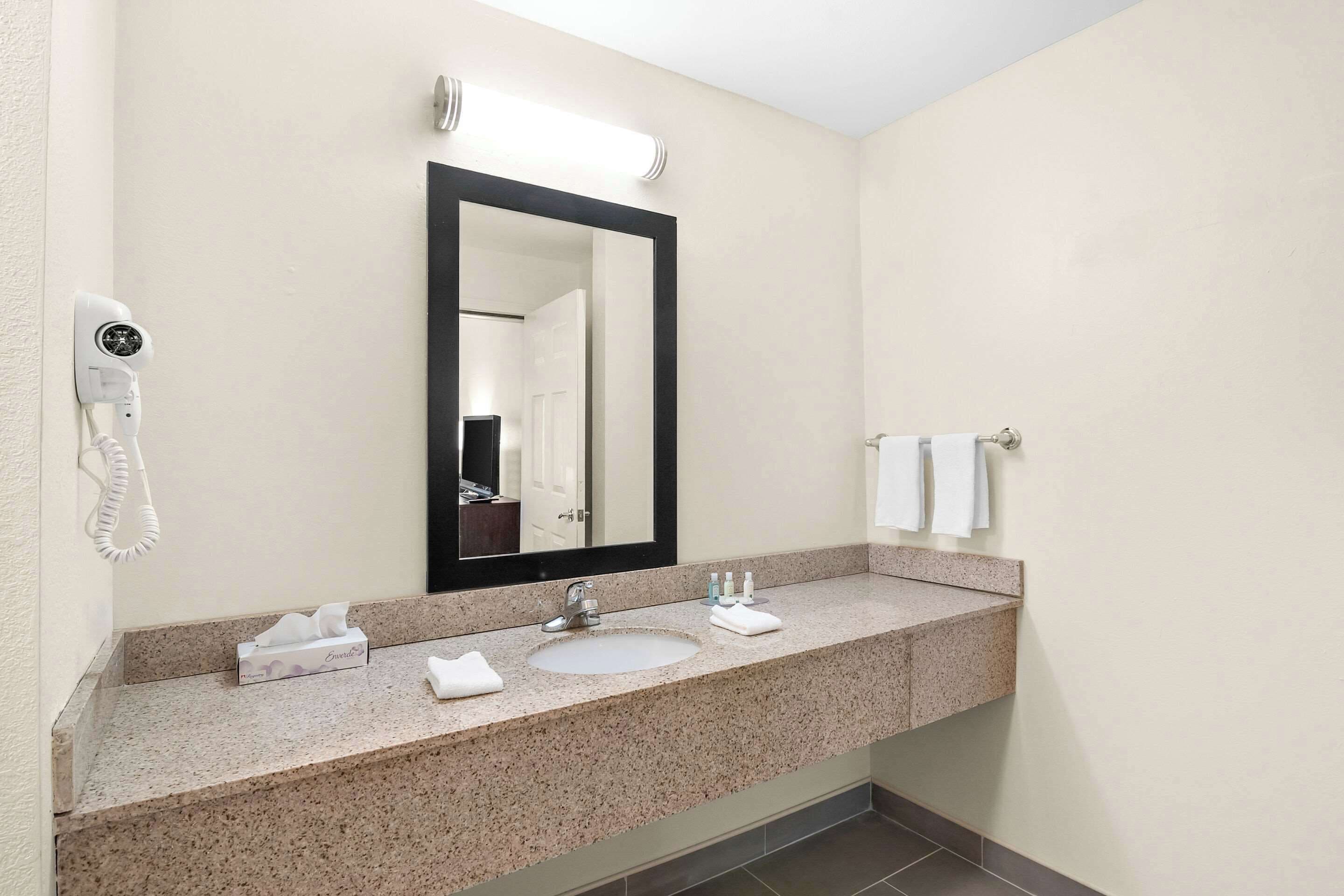 Un baño con lavamanos, espejo, toallero y una cámara de seguridad.