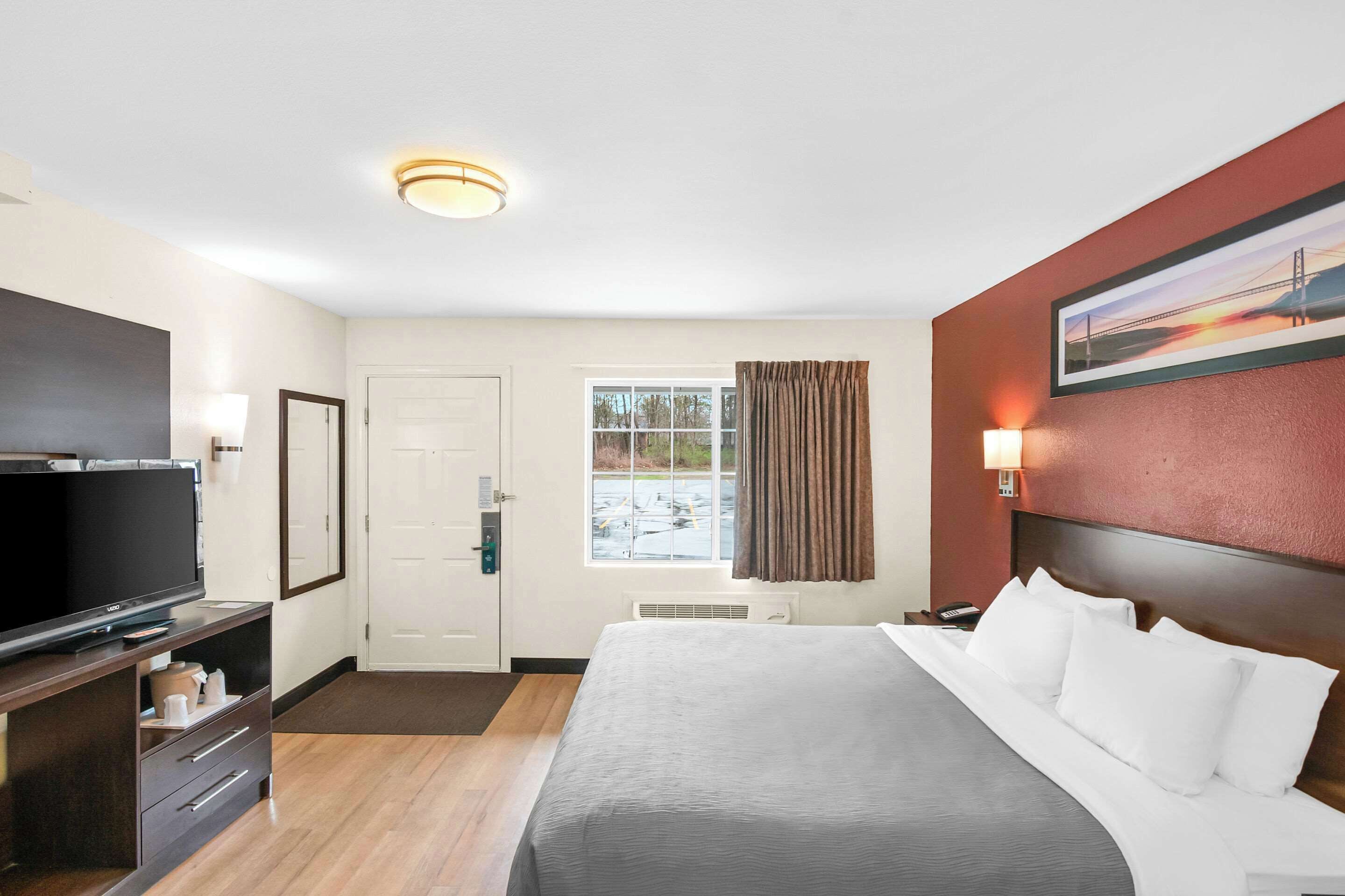 Une chambre d’hôtel avec un lit, une télévision, un bureau avec une lampe, une porte et une fenêtre avec des rideaux.