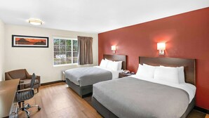 Ein Hotelzimmer mit zwei Betten, einem Schreibtisch und einem Stuhl.