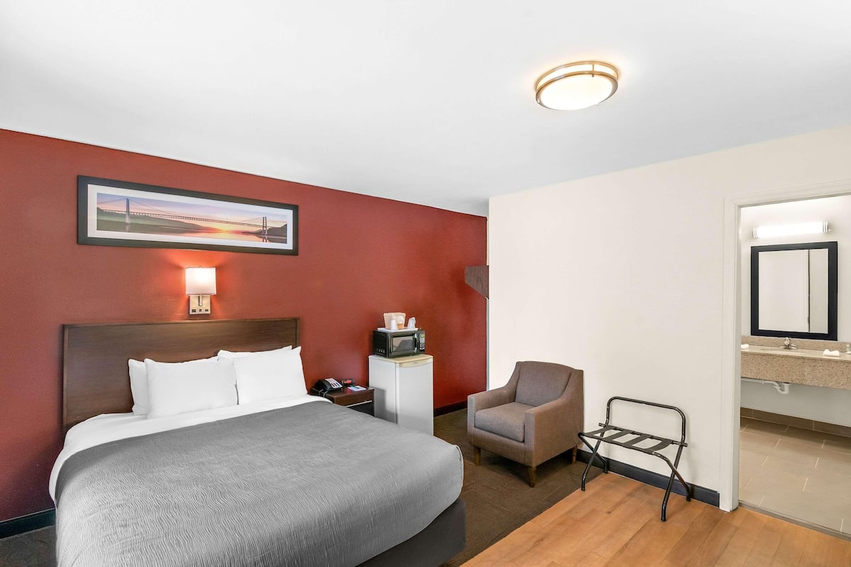A hotel room with a bed, a chair, a small table, a microwave, and a picture on the wall.